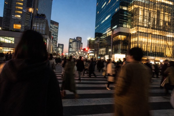 Small group crossing the Shibuya scramble at street level with neon signs rising on every side