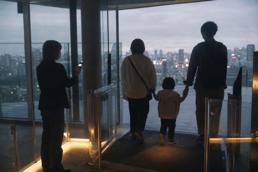Family walking through the glass entrance gates of a rooftop observation deck while a staff member scans a phone screen