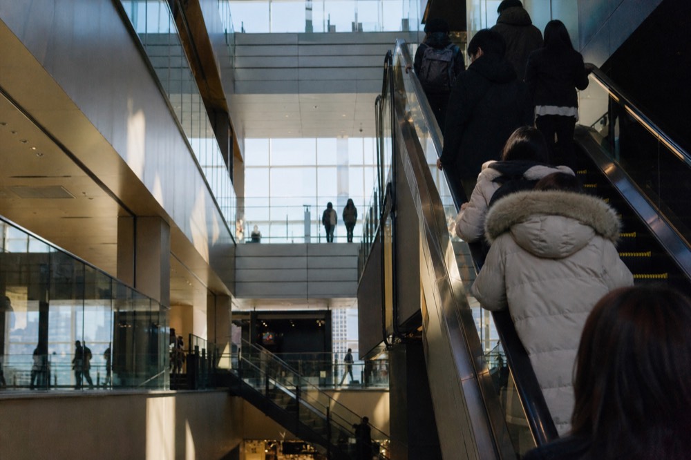 Escalators rising through a bright multi-level shopping atrium inside a Tokyo tower with shoppers on several floors