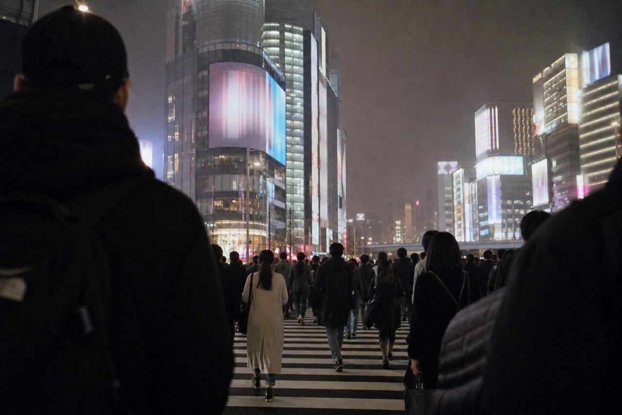 Crowds converging from every direction across a wide Tokyo intersection beneath tall illuminated advertising screens at night