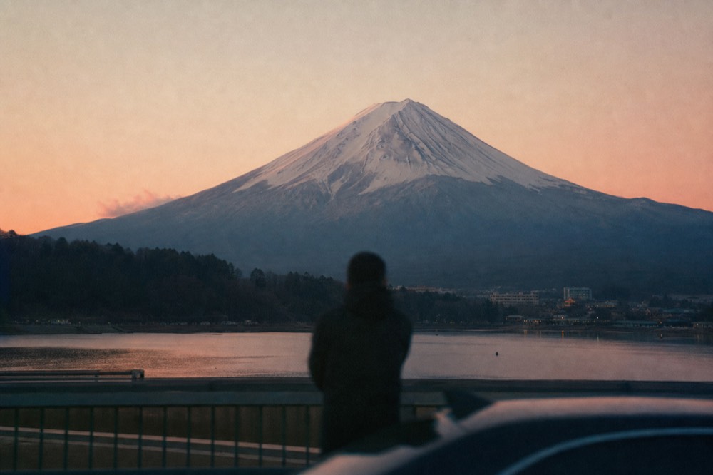 Large snow-covered volcano rising directly above a calm lake and low pine forest on a clear cold morning