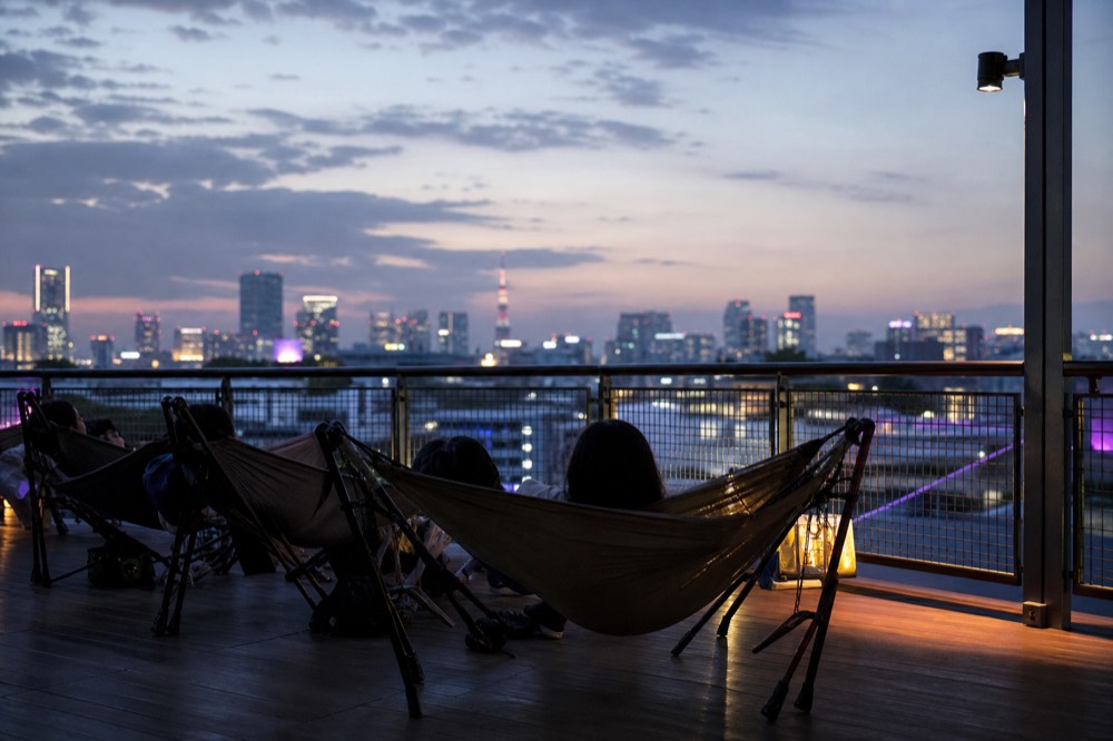 Visitors lying back in low hammocks on an open rooftop deck at dusk with the sky darkening overhead and no glass in view