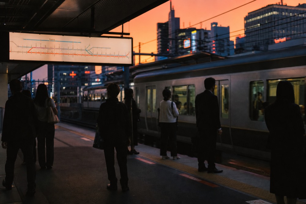 Tokyo subway platform with a train arriving, route map panel above the doors and commuters waiting behind yellow floor markings