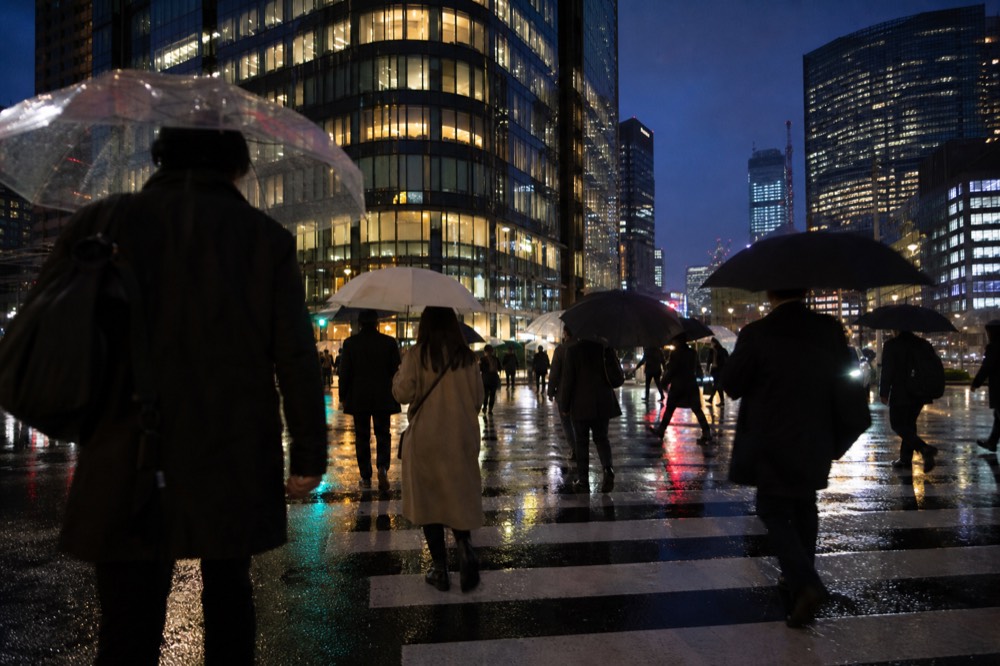Crowd of pedestrians with umbrellas crossing a wet city intersection at night with reflected neon on the asphalt